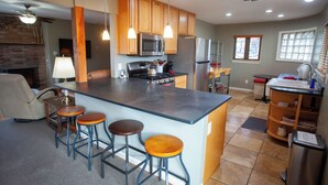 Cocina moderna con una isla central, taburetes de bar, armarios de madera, electrodomésticos de acero inoxidable e iluminación colgante.