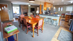 Un comedor amplio con una mesa y sillas de madera, una cocina al fondo y una chimenea.