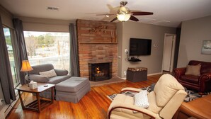 Una sala de estar con chimenea, ventilador de techo, sofá, sillón reclinable y televisor.