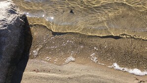Una vista despejada de una playa arenosa con ondulaciones en el agua y una roca grande al frente.