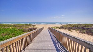 Une promenade en bois qui mène à une plage bordée de dunes et offrant une vue sur l’océan.