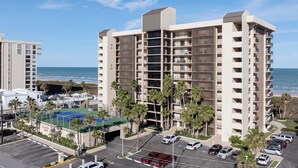 Un hôtel de grande hauteur doté de nombreux balcons, d’un parking et d’un court de tennis.