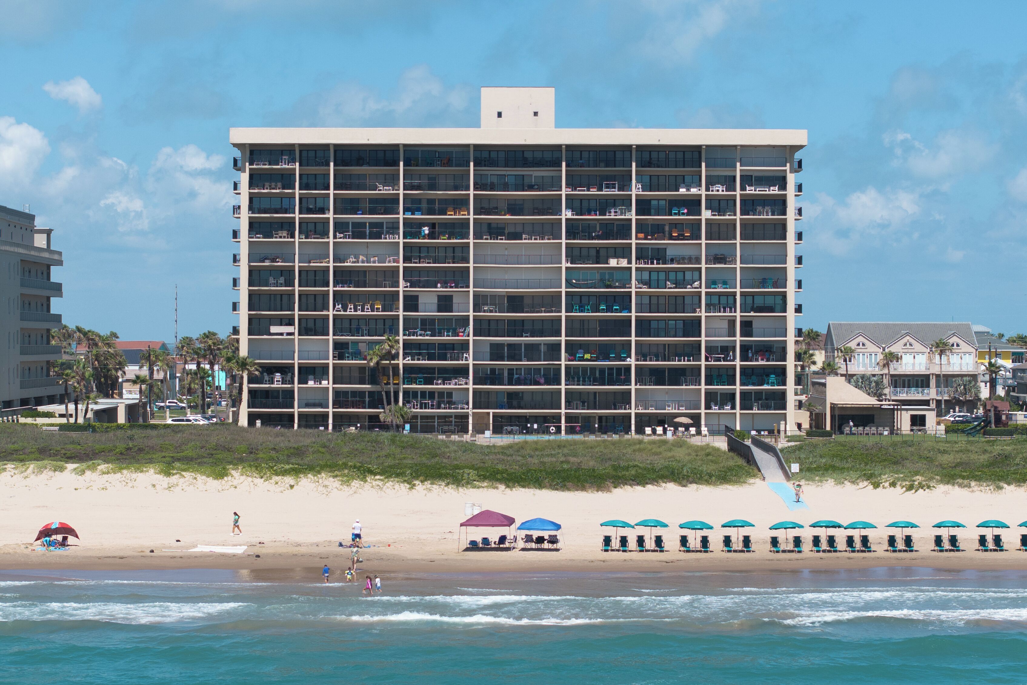 Ein mehrstöckiges Hotel mit Blick auf den Strand, gelegen am sandigen Ufer mit Pool und Sonnenschirmen.
