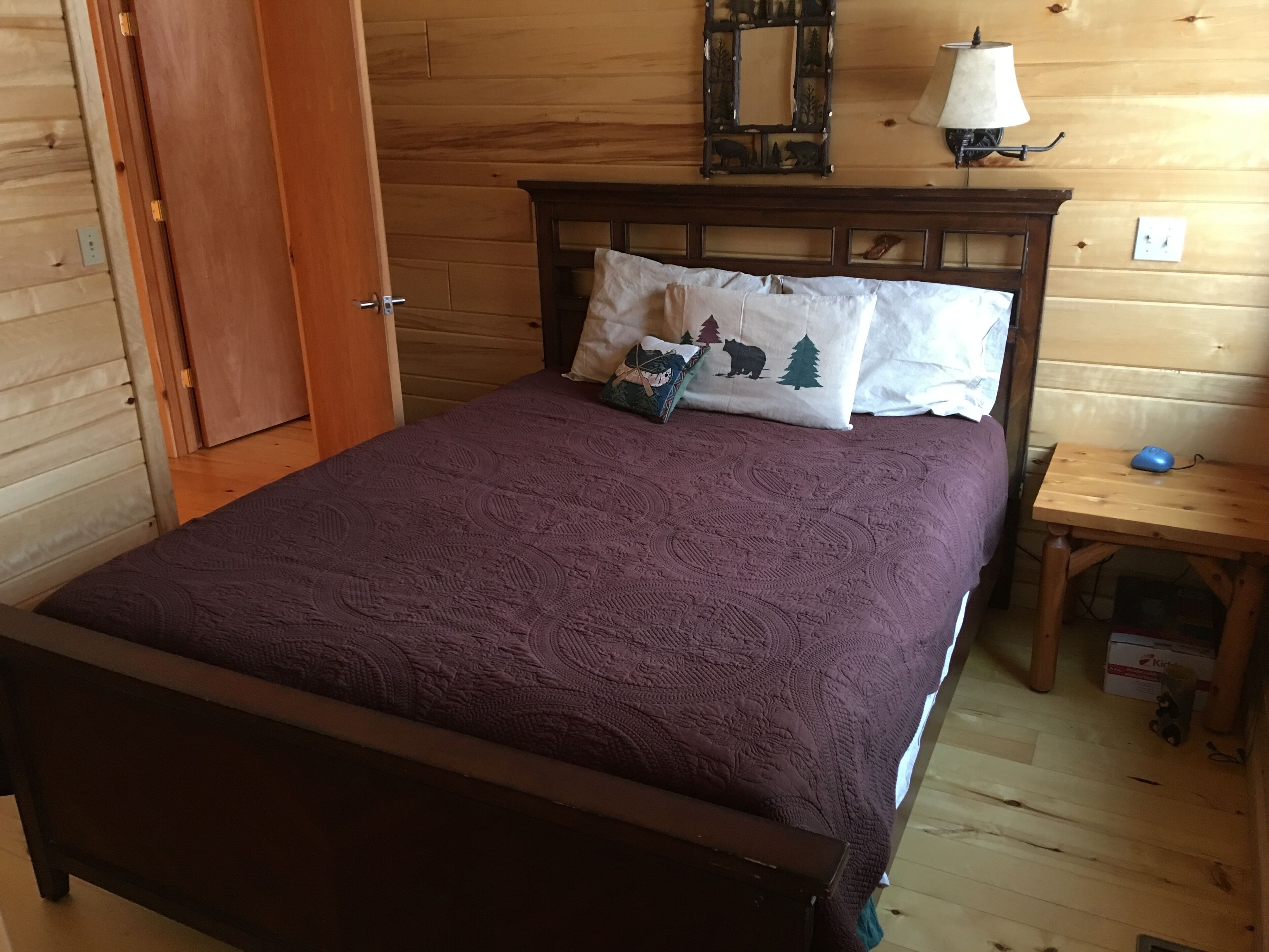 Una habitación con paneles de madera, una cama, una mesita de noche, una lámpara y un espejo.