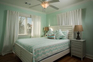 Une chambre à coucher avec un lit, une table de chevet, un ventilateur de plafond et une fenêtre avec des rideaux.