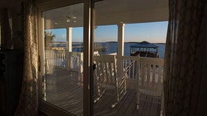 A wooden deck with white railings and a glass door leading to a view of the water. - Beach Front South End, Designer Decorated, Dream Retreat on Tybee Island! (Tybee Island)