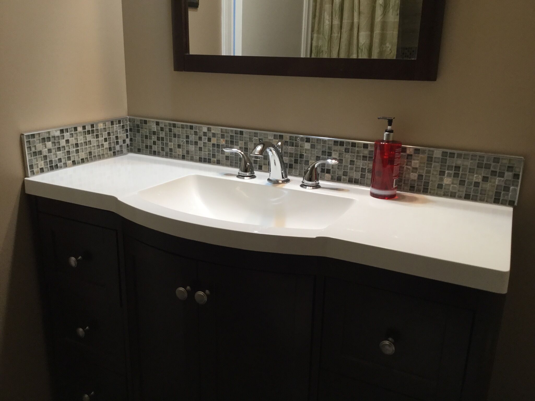 Un baño con un lavabo blanco, dos grifos, un espejo sobre el lavabo y un salpicadero de azulejos.