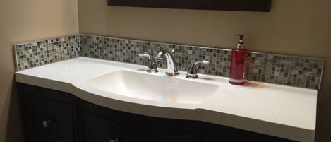 Un baño con un lavabo blanco, dos grifos, un espejo sobre el lavabo y un salpicadero de azulejos.