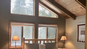 A bedroom with a wooden bed, two bedside tables, and large windows.