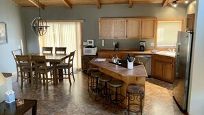 A spacious kitchen with wooden cabinets, a large island with stools, a dining area with a table and chairs, and a modern refrigerator.