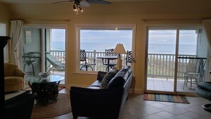 Un salon avec un canapé, une table basse en verre et un fauteuil. Il y a un balcon avec vue sur l’océan.