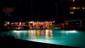 Ein beleuchteter Poolbereich mit Liegestühlen und einer Bar.