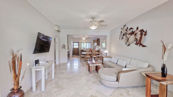 A spacious living room with a white sofa, a TV, and a ceiling fan. - one block to medano beach , 2 blocks to the Cabo Marina & Downtown Cabo (Cabo San Lucas)