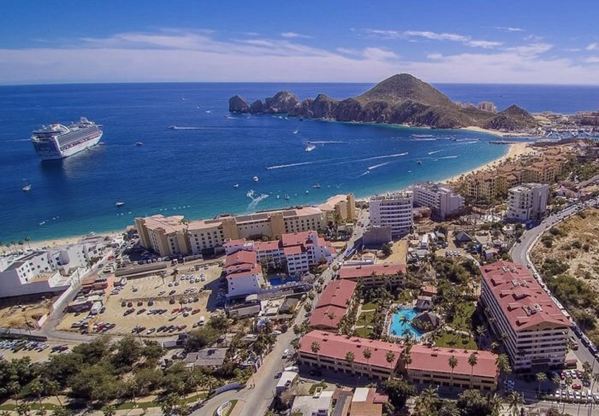 Ein Küstenort mit mehreren Hotelgebäuden, einem Strand und einem Kreuzfahrtschiff im Hintergrund.