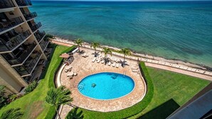 Un hotel con piscina circular rodeada de palmeras y sillas de descanso, con vista a un océano azul y despejado.