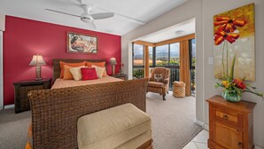 Un dormitorio con cama, una silla, una mesita de noche, lámpara, un cuadro y vistas al exterior.