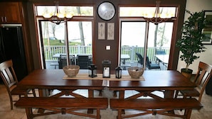 Un coin repas avec une table et des bancs en bois, une horloge au mur et une vue sur une terrasse extérieure.