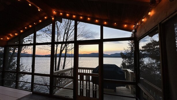 A covered deck with a view of a lake and mountains at sunset.