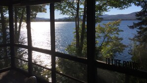 A view through a window with a grid pattern, overlooking a calm lake surrounded by trees and distant hills.