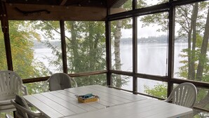 A covered outdoor dining area with a white table and chairs, overlooking a lake.