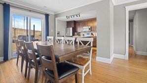 Un vaste espace de salle à manger avec une table et des chaises en bois, une cuisine dotée de meubles en bois et une vue dégagée grâce à de grandes portes-fenêtres coulissantes.