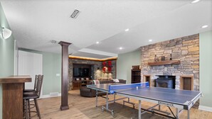 Une table de ping-pong dans un salon, avec une cheminée en pierre et un téléviseur en arrière-plan.