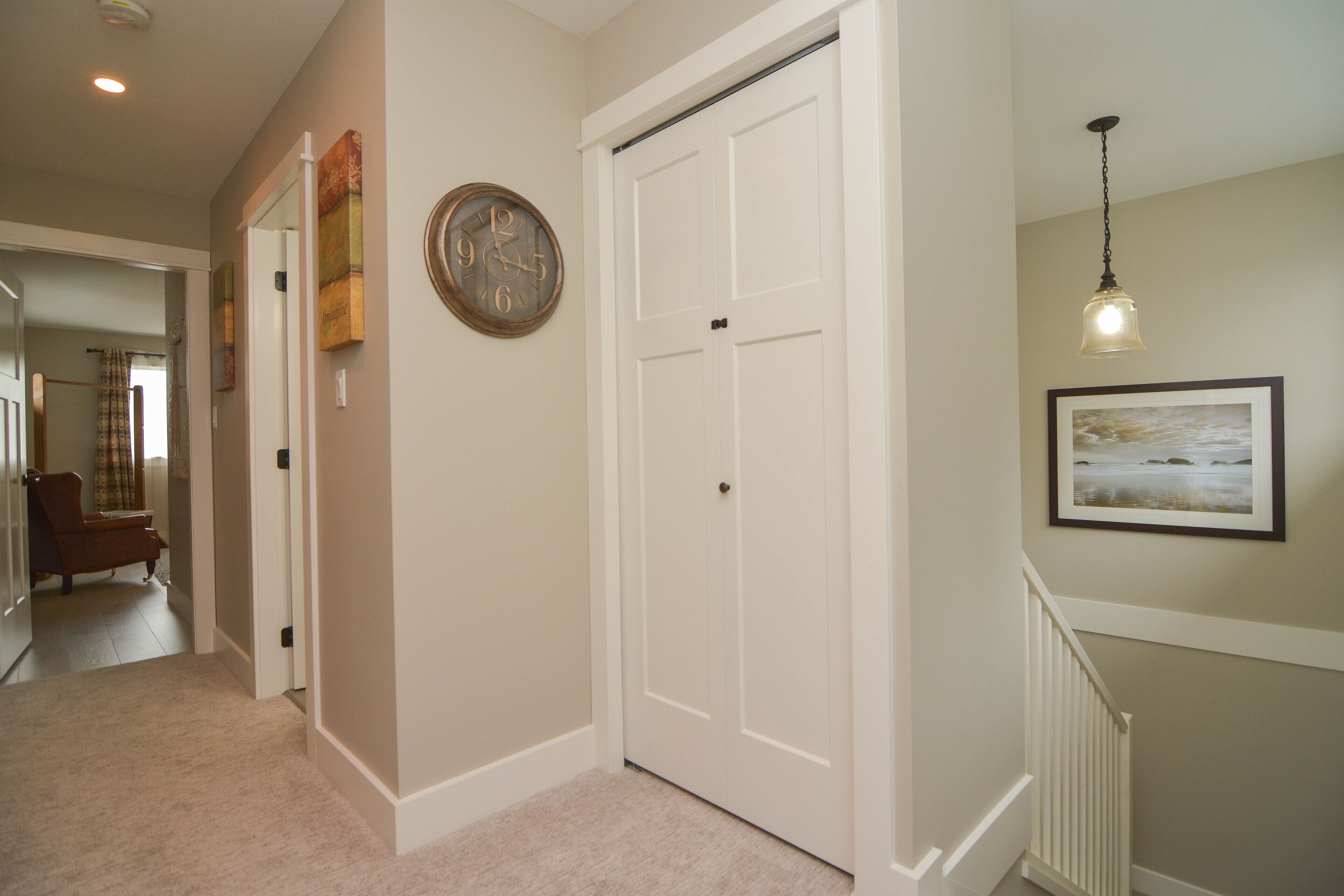 Un couloir avec une porte blanche fermée, une horloge et un tableau encadré accroché au mur.