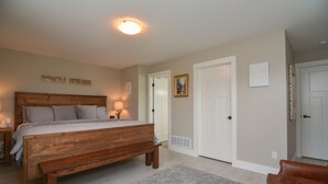 A bedroom with a wooden bed, a nightstand, a lamp, a bench, and a gray rug.