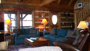 Interior acogedor de una cabaña de madera con dos sofás, una mesa de centro y un pouf estampado.