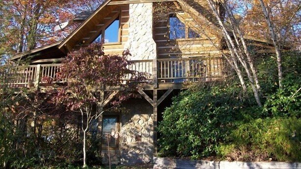 Una cabaña de madera con chimenea de piedra, un balcón y un muro de piedra.