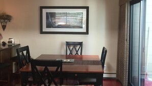 A dining area with a wooden table and chairs, a framed picture on the wall, and a window with curtains.