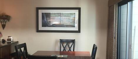 A dining area with a wooden table and chairs, a framed picture on the wall, and a window with curtains.