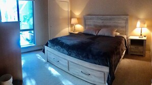 Un dormitorio con una cama grande, dos mesitas de noche con lámparas, una ventana con vistas y una puerta.