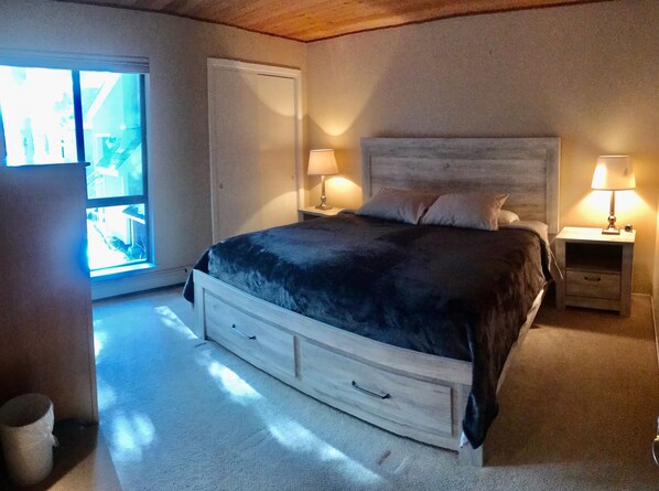 A bedroom with a large bed, two bedside tables with lamps, a window with a view, and a door.