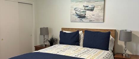 A bedroom with a bed, two bedside tables, a ceiling fan, a painting, and a door.