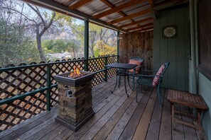 A wooden deck with a stone fire pit, two chairs, and a table.