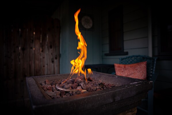 A fireplace with burning logs and flames, a wooden fence, and a clock on the wall.