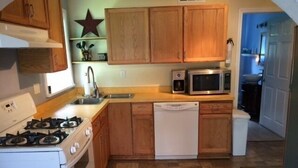 A compact kitchen with wooden cabinets, a microwave, a dishwasher, and a gas stove. - Conesus Lake Cottage Rental (Conesus)