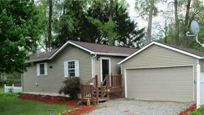 A single-story house with a front porch, a garage, and a gravel driveway. - Conesus Lake Cottage Rental (Conesus)