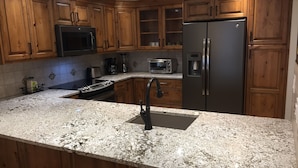 A kitchen with wooden cabinets, a stainless steel refrigerator, a microwave, a toaster, and a granite countertop. - Need an escape from summer heat? Cool down in our cozy condo! Summer dates open! (Breckenridge)