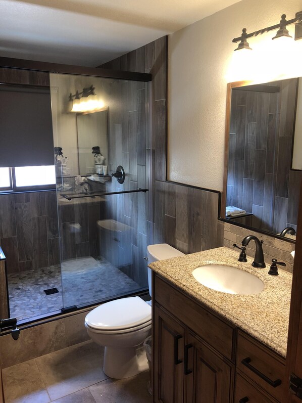 A modern bathroom with a glass-enclosed shower, a white toilet, and a granite countertop sink. - Need an escape from summer heat? Cool down in our cozy condo! Summer dates open! (Breckenridge)