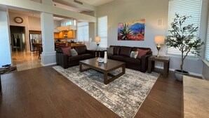 A spacious living room with a dark wood floor, a central coffee table, two sofas with cushions, a dining area in the background, and a ceiling fan. - Desert Retreat - 4BR/3BA Heated Pool & Spa - Recently Renovated - Monthly Rental (Scottsdale)