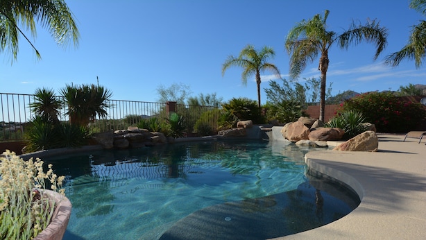 A swimming pool with clear water, surrounded by rocks and palm trees. - Desert Retreat - 4BR/3BA Heated Pool & Spa - Recently Renovated - Monthly Rental (Scottsdale)