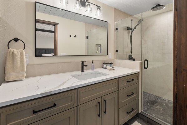Une salle de bain moderne avec un grand miroir, un lavabo et un espace douche.