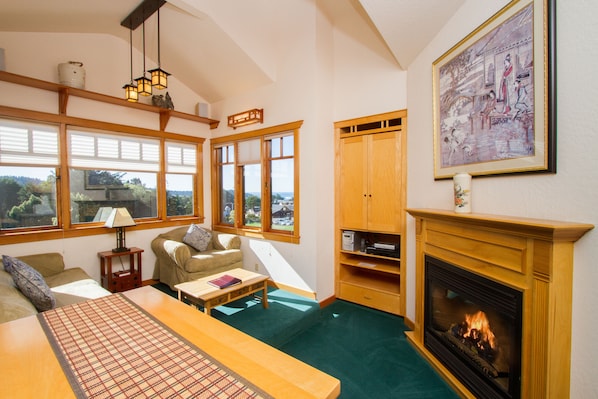 A cozy living room with a fireplace, large windows, and a view of the outdoors. - Ocean View King Suite in Mendocino Village with Free Wi-Fi and Jacuzzi Bathtub (Mendocino)
