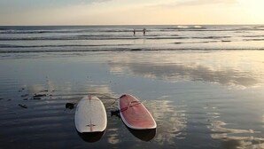 To surfboards på en våd strand med bølger i baggrunden.