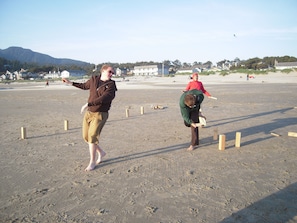 Uma praia arenosa com duas pessoas brincando com pipa.