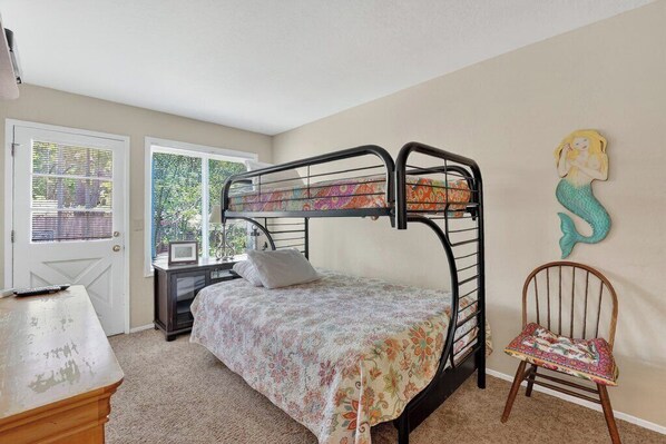 A bunk bed room with a door, a chair, and a mermaid decoration on the wall. - Boardwalk Beach House (Santa Cruz)