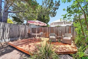 A wooden deck with outdoor furniture, including chairs and a table, surrounded by a wooden fence and trees.