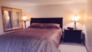 A bedroom with a bed, two bedside tables with lamps, a window with blinds, and a wall-mounted mirror. - Newly Remodeled 2Bd, 2Ba/ Steps From The Super B-lift /ski rental/restaurant/bus (Frisco)